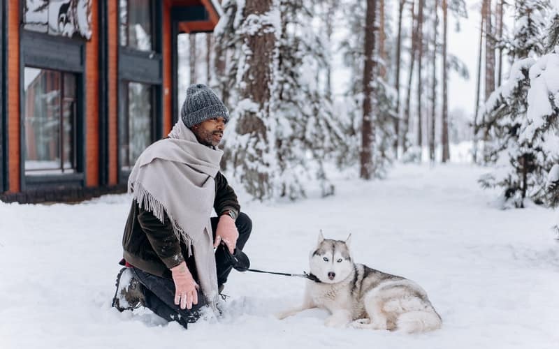 a man kneeling in the snow with his husky dog